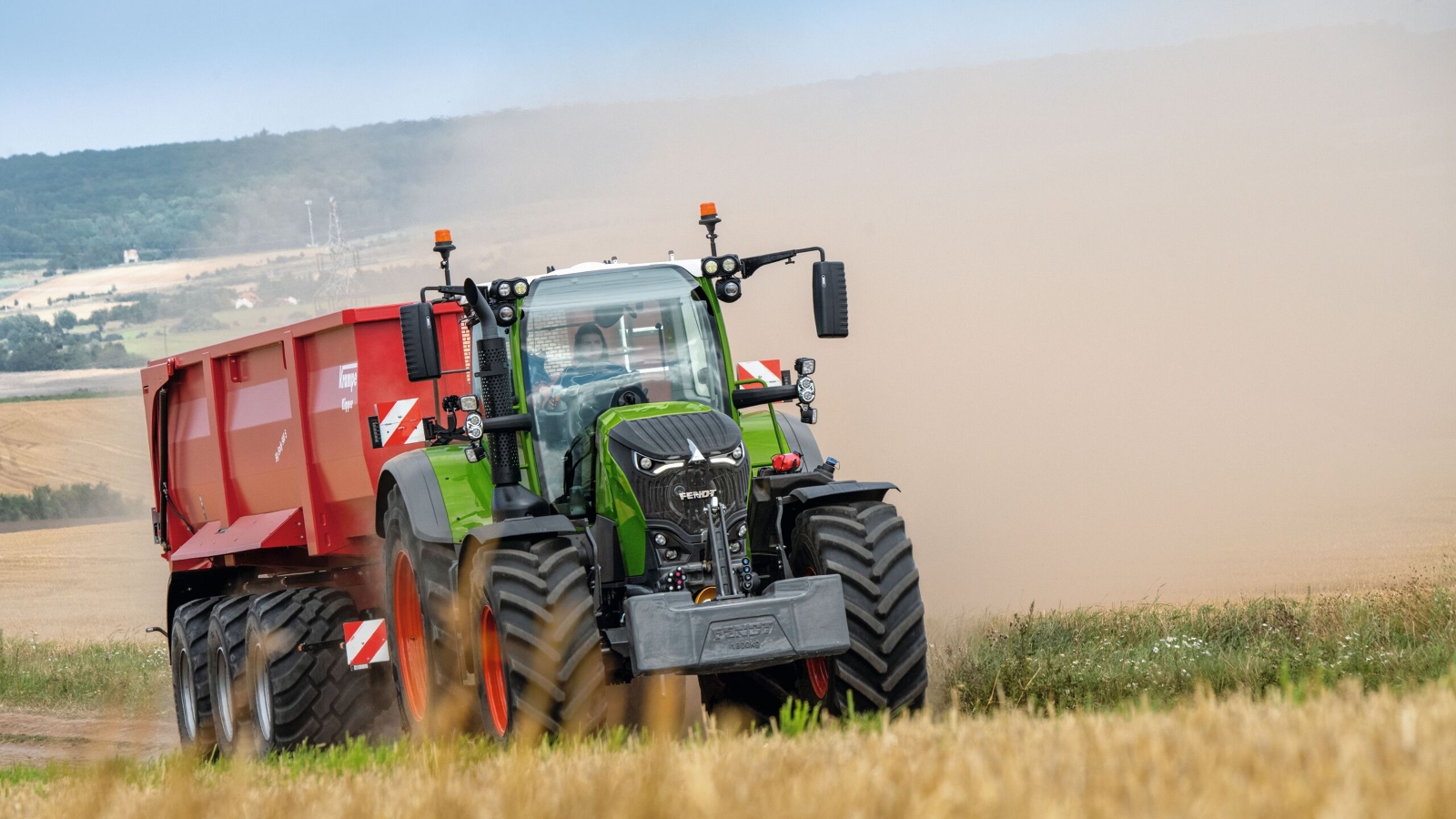 Een boer rijdt met een Fendt 700 Vario Gen7 en een rode kipper op een akker.
