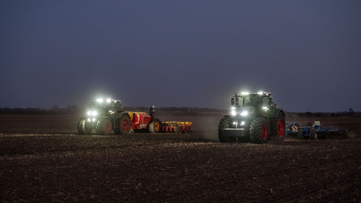 De Fendt 1000 Vario en de Fendt 800 Vario werken in het donker samen op een veld met ingeschakelde schijnwerpers.