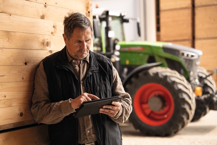 Mann ser på iPad med en Fendt-traktor i bakgrunnen