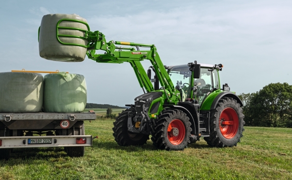 Fendt 600 Vario med frontlaster som løfter rundballer opp på en tilhenger