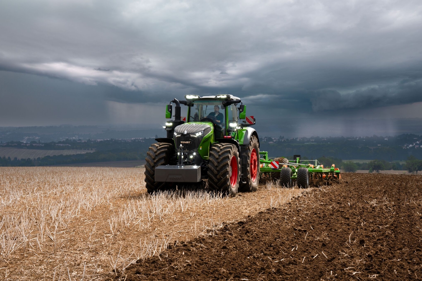 Fendt 1000 Vario traktor arbeider på et jorde - med tunge uværsskyer i bakgrunnen