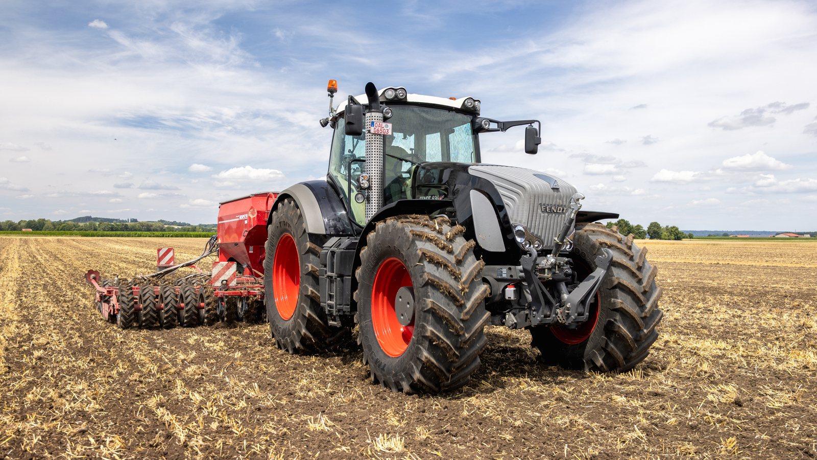 En jordbruker kjører en svart-grå Fendt 936 Vario på en åker, og en maisåker kan ses i bakgrunnen