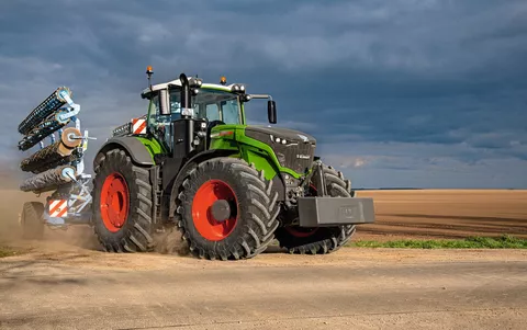 Fendt 1000 Vario z narzędziem na drodze obok pola