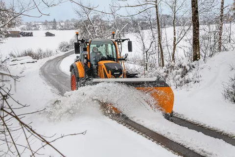 Pomarańczowy ciągnik Fendt odśnieżający drogę w zaśnieżonym krajobrazie