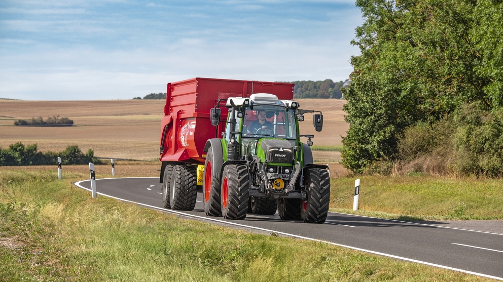 Rolnik na drodze z ciągnikiem Fendt 200 Vario i przyczepą samozaładowczą