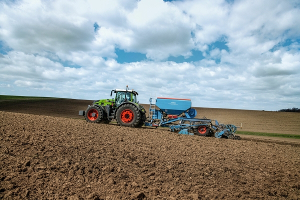 Fendt 900 Vario z agregatem siewnym Lemken Ciągnik Fendt 900 Vario z agregatem siewnym Lemken podczas siewu na polu. W tle rozpościera się rozległy krajobraz pól uprawnych pod częściowo zachmurzonym niebem.