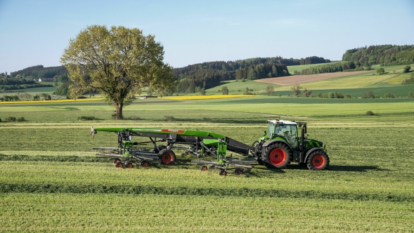 Fendt Former 14055 PRO Zielony ciągnik Fendt z czerwonymi obręczami kół i doczepioną zgrabiarką Fendt Former 14055 PRO podczas pracy na zielonym letnim polu.