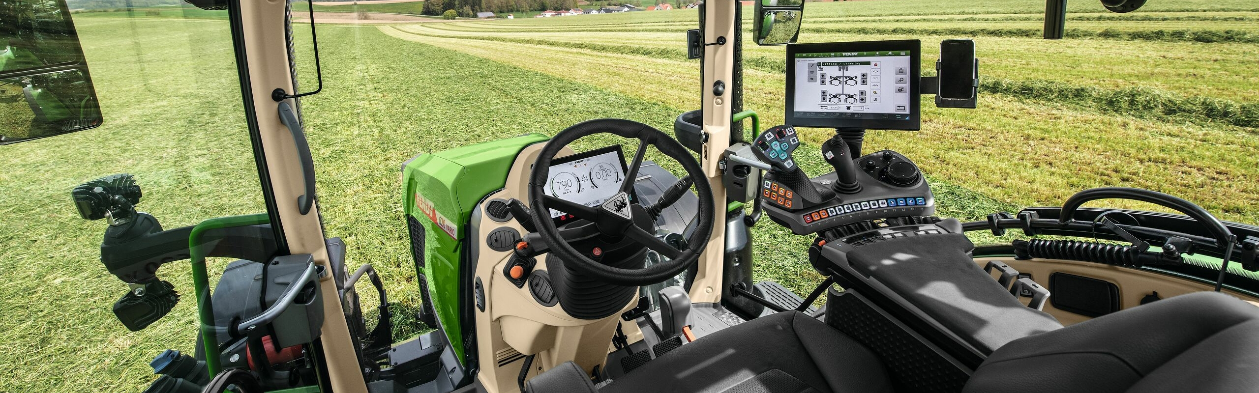 Widok wnętrza kabiny ciągnika Fendt 600 Vario, w tle zielona łąka.