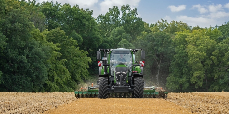 Zielony ciągnik Fendt 600 Vario uprawiający glebę na polu z lasem w tle