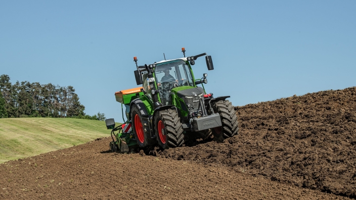 Fendt 500 Vario z agregatem siewnym na polu Zielony Fendt 500 Vario przejeżdża przez pole z agregatem siewnym Amazone w kolorze zielono-pomarańczowym i przeprowadza wysiew.