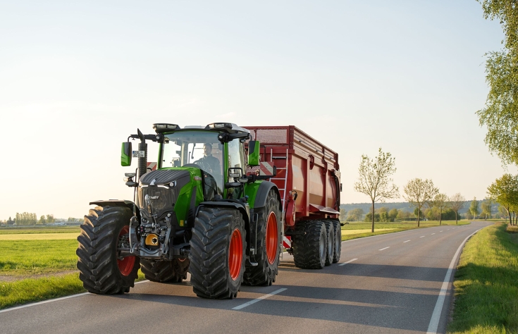 Fendt 800 Vario w transporcie drogowym Zielony ciągnik Fendt 800 Vario jedzie drogą z czerwoną przyczepą firmy Krampe.