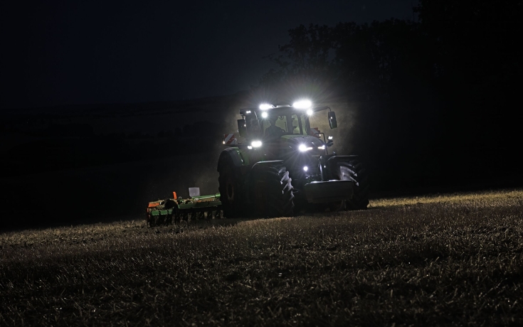 Ciągnik Fendt 800 Vario z włączonymi reflektorami UltraVision Ciągnik Fendt 800 jedzie po polu w ciemności z włączonymi reflektorami, ciągnąc bronę talerzową.