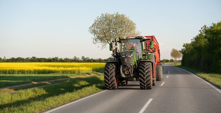 Ciągnik Fendt 800 Vario podczas transportu drogowego z przyczepą Zielony ciągnik Fendt 800 Vario drogą z czerwoną przyczepą firmy Krampe.