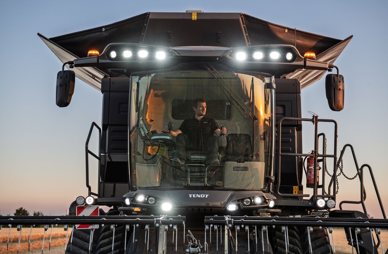 Zbiór zboża za pomocą kombajnu zbożowego Fendt IDEAL Widok czarnego kombajnu zbożowego Fendt IDEAL podczas żniw na polu zboża z włączonymi reflektorami