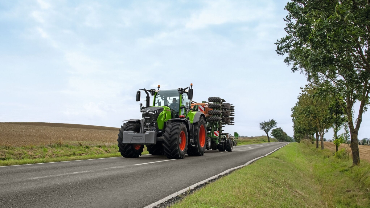 Rolnik kierowca ciągnika Fendt 700 Vario Gen7 z elementem roboczym na drodze.