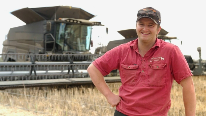 Retrato de Ben Beech con camisa roja y gorra en un campo, delante de dos Fendt IDEAL y un cielo azul