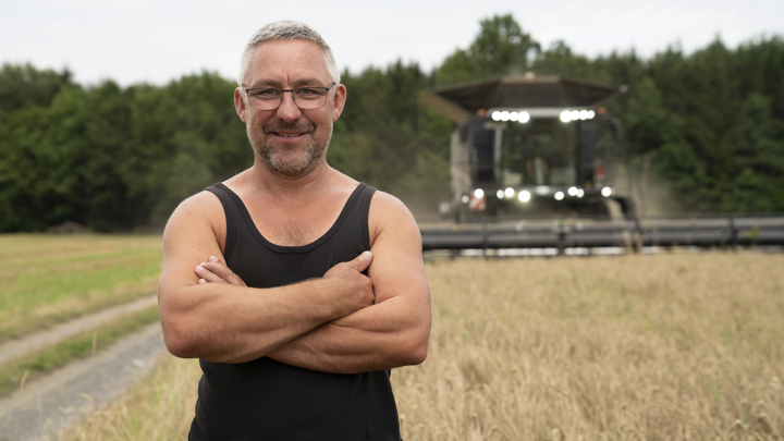 Retrato de Heiko Hölzel delante de un campo junto a un bosque, con una cosechadora Fendt IDEAL al fondo