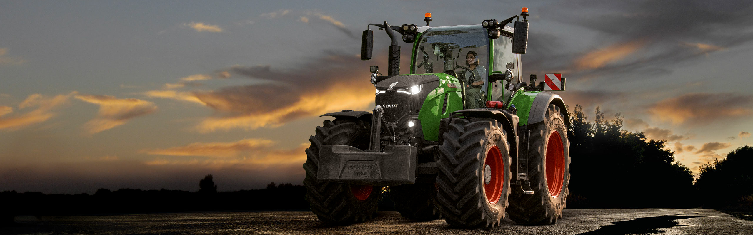 En Fendt 700 Vario Gen7 på vägen framför en dramatisk solnedgång