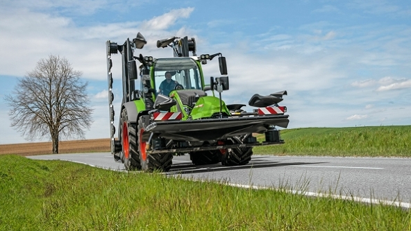 Transportläge Grön Fendt-traktor som kör på en landsväg med infälld lyftanordning.