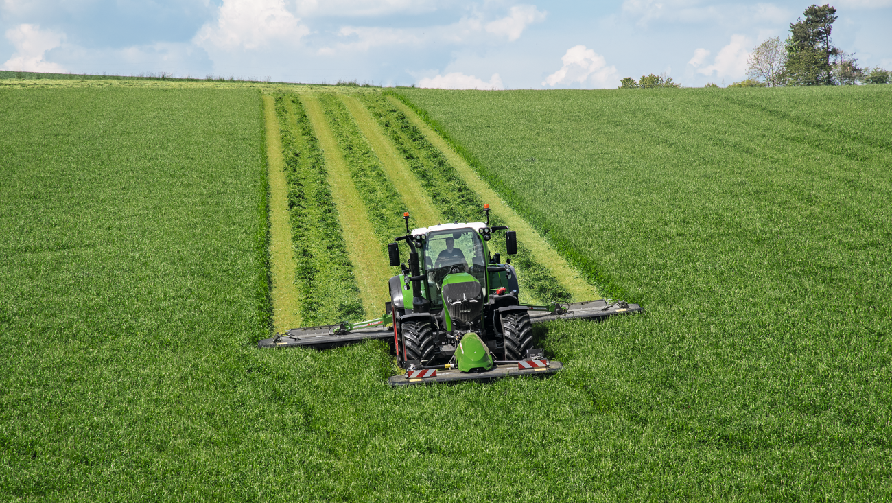 En lantbrukare klipper en äng med en Fendt Slicer front- och bakmonterad slåttermaskin.