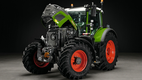 Den gröna Fendt 600 Vario med röda fälgar står med öppen motorhuv på ett grått golv. Bakgrunden är svart.
