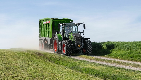 Den gröna Fendt 600 Vario-traktorn med röda fälgar och den gröna Fendt Tigo-självlastarvagnen kör längs en liten åkerväg med en grön äng i förgrunden och bakgrunden.