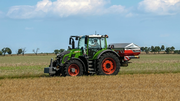 Den gröna Fendt 600 Vario-traktorn med röda fälgar sedd från sidan på en grön äng. I bakgrunden syns en blå himmel med vita moln.
