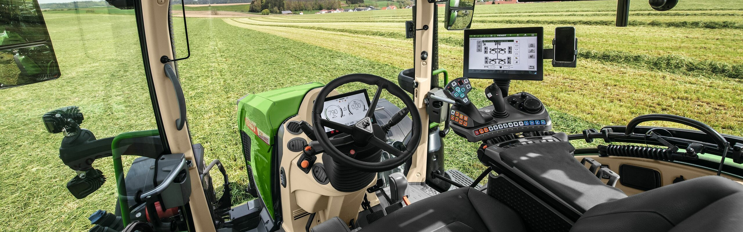 Invändig vy av förarhytten på Fendt 600 Vario med utsikt över en grön äng.