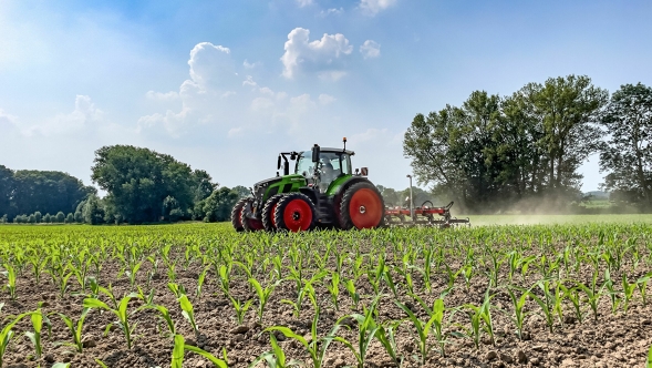 Den gröna Fendt 600 Vario-traktorn med tvillingdäck används på ett odlat fält. I bakgrunden syns mörkgröna träd och en ljusblå himmel med vita moln.