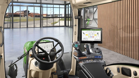 Vy över hytten VisioPlus på en Fendt 300 Vario Gen5 med ergonomisk kontrollarm, ratt och stor terminal framför en modern innergård med glasfasad.