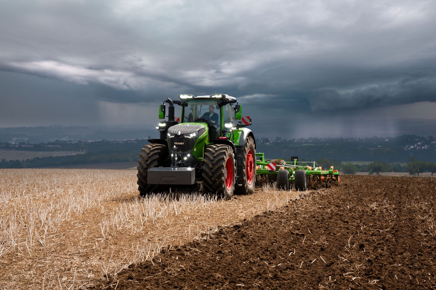 Fendt 1000 Vario-traktorn utför fortfarande kraftfullt sitt fältarbete framför tunga, hotande orosmoln i fjärran