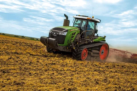 Зелений Fendt 1100 MT з червоними дисками і червоним навісним обладнанням під час польових робіт на коричневому полі з зеленими луками і блакитним небом на задньому плані.