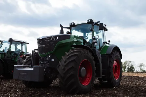 Вигляд спереду великого зеленого трактора Fendt з червоними колесами на стерні на тлі блакитного неба і хмар