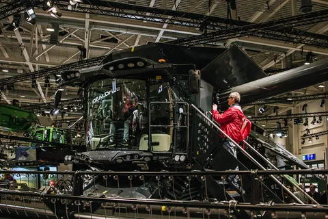 Відвідувачі виставки Agritechnica стоять біля великого чорного Fendt IDEAL у виставковому залі та роблять фотографії.