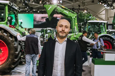 Чоловік у сорочці та піджаку стоїть на виставці Agritechnica перед безліччю різних машин марки Fendt на виставковому стенді Agritechnica.