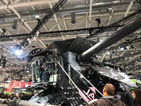 Відвідувачі виставки Agritechnica стоять біля великого чорного Fendt IDEAL у виставковому залі та роблять фотографії.