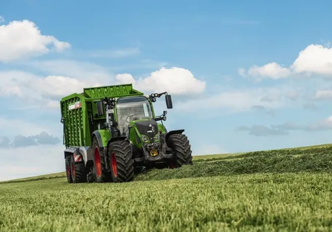 трактор Fendt, що їде по зеленому полю з причепом Fendt Tigo