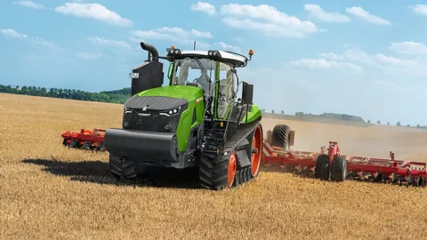 Вигляд спереду трактора Fendt 1100 MT Vario, який працює з червоним навісним обладнанням на полі з залишками врожаю. На задньому плані видно блакитне небо з поодинокими хмарами та зелений ліс.