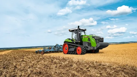 Бічний вигляд Fendt 1100 MT Vario із зеленим навісним обладнанням на полі з пожнивними рештками. На задньому плані видно зелений ліс і блакитне небо з розсіяними хмарами.