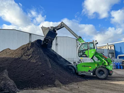 A telehandler is using its bucket to tip soil onto a large pile.