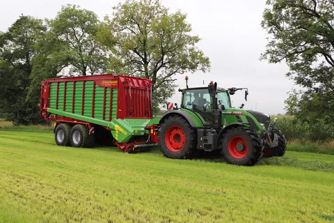 A Fendt tractor drives across a grass field with a Strautmann loader wagon attached, loading grass