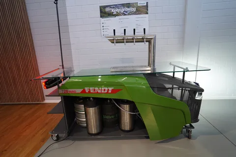 Fendt drinks dispenser (side view) with Fendt logo, castors, 4 taps, a glass shelf and front and rear lights switched on.
