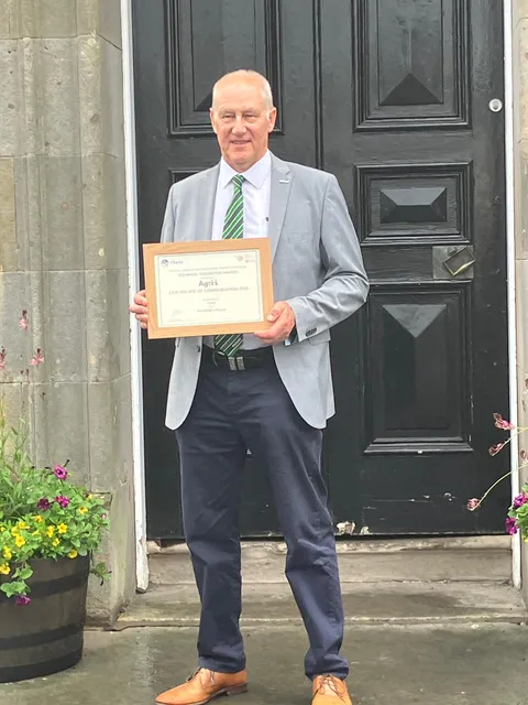 A man holds a certificate in his hands standing in front of a black door