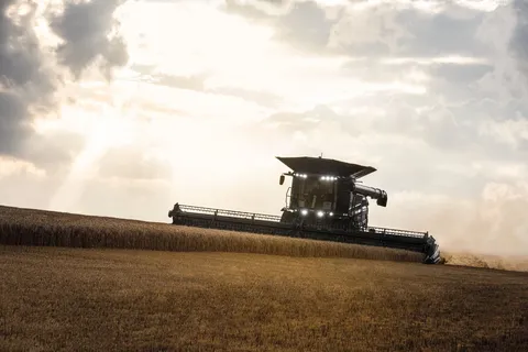 A Fendt IDEAL combine harvester driving head-on towards the camera and threshes wheat in the early evening. The spotlights are switched on.
