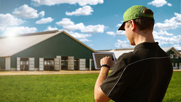 A farmer with a tabler stands in front of his farm and subscribes to the newsletter