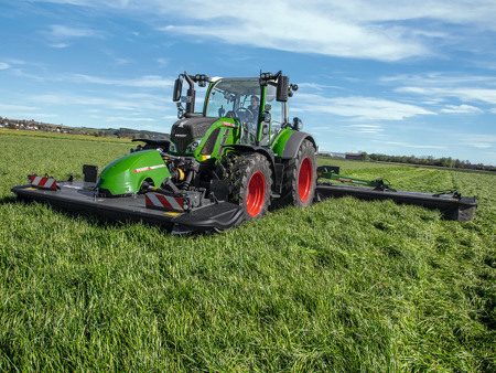 A farmer drives his tractor and a Fendt Slicer mower in the meadow