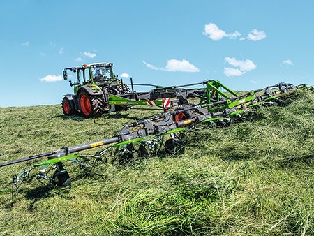 A farmer drives his tractor and a Fendt Lotus tedder in the meadow