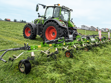 A farmer drives his tractor and a Fendt Twister tedder in the meadow