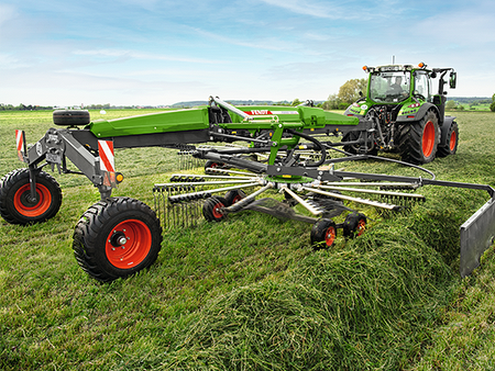 A farmer drives his tractor and a Fendt Former rake in the meadow