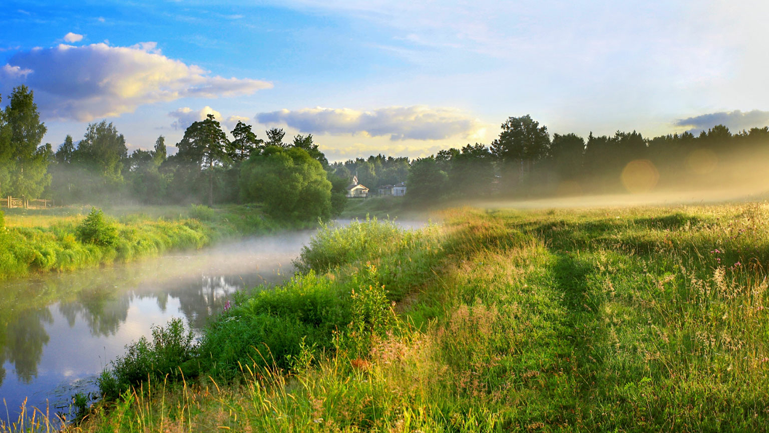 Grassland at dawn with a small river and the sun